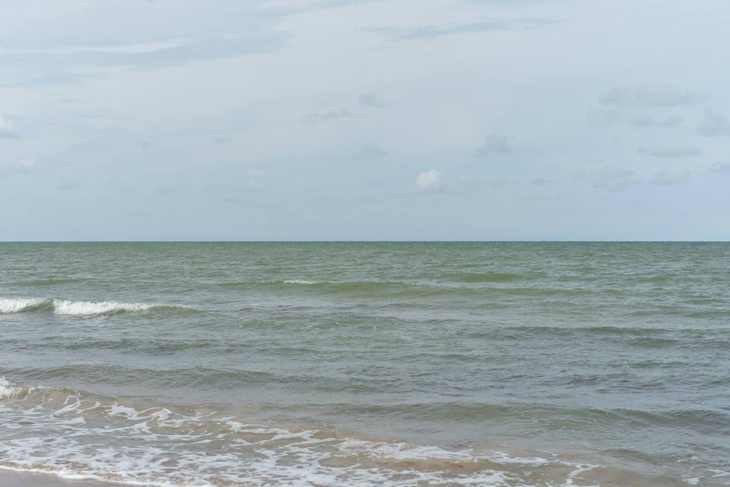 Gentle waves wash onto the sandy beach under a cloudy sky.