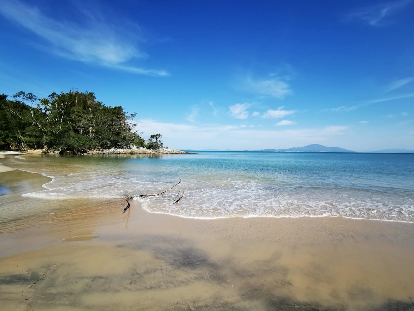 Gentle waves wash onto a sandy beach near a rocky cliff.