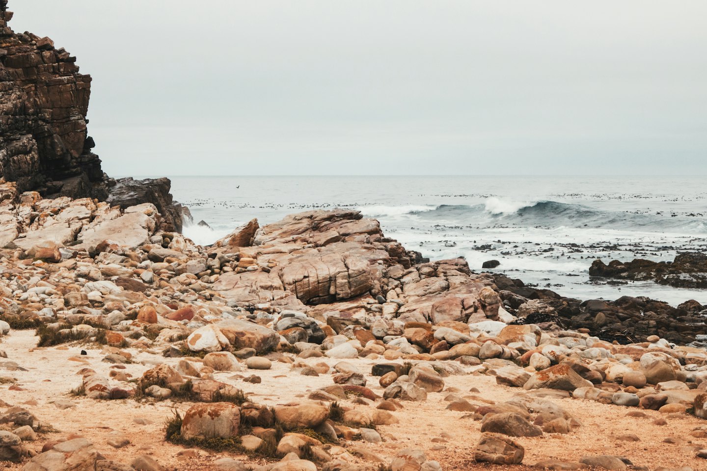 Waves break against a rugged brown cliff and rocky shoreline.