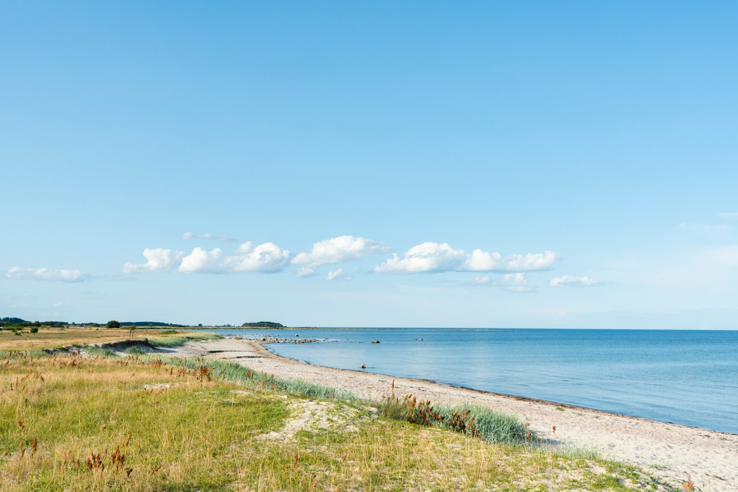 Sandy beach with dunes and calm blue sea.