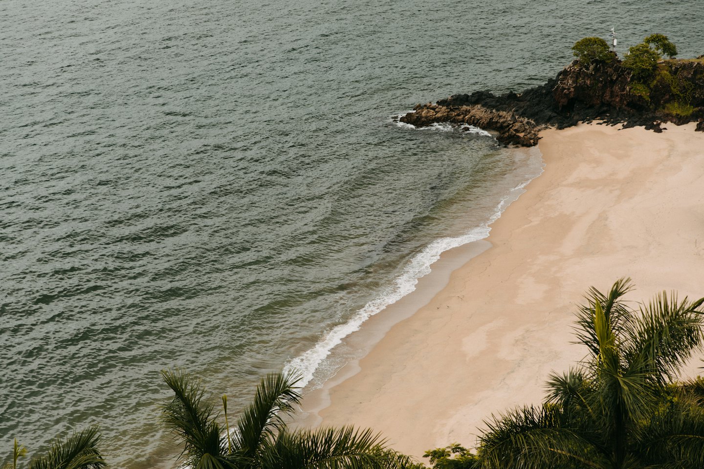 Aerial view of a sandy beach with gentle waves and a rocky headland.