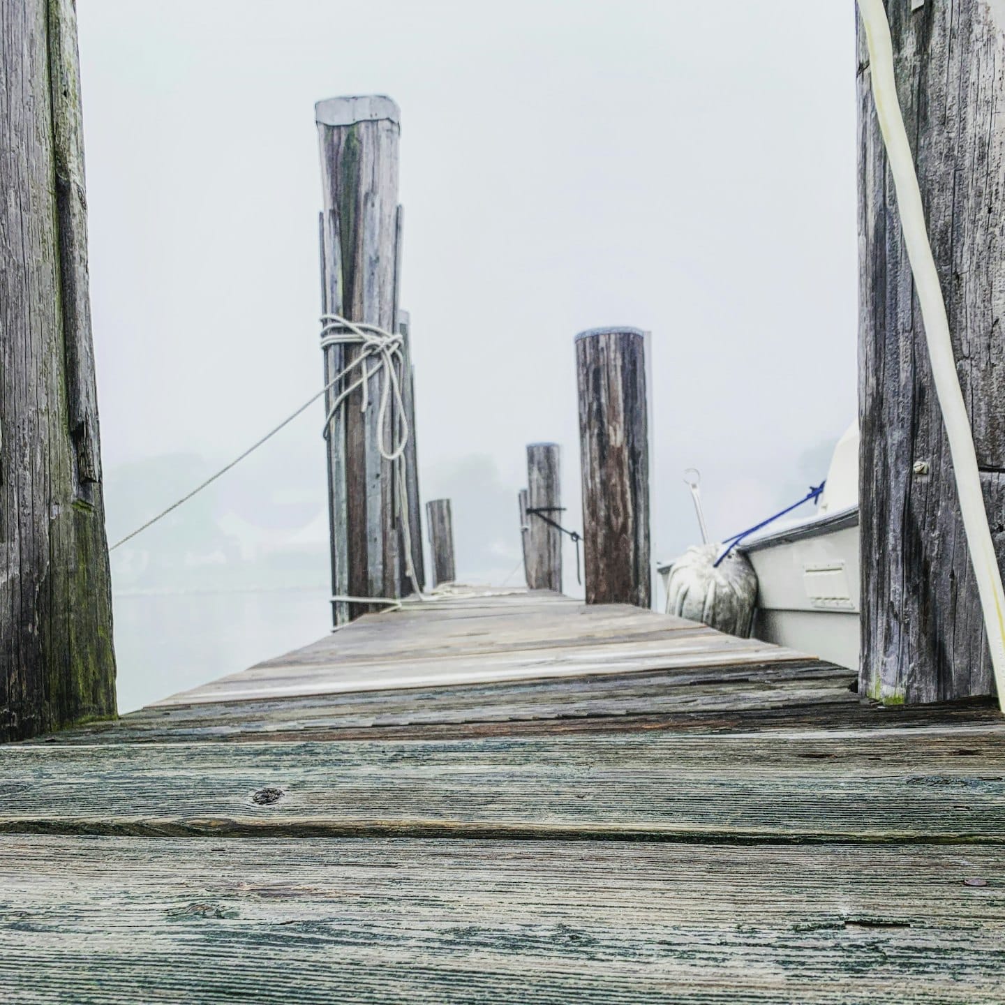 Weathered wooden dock disappearing into thick fog with a small boat tied.