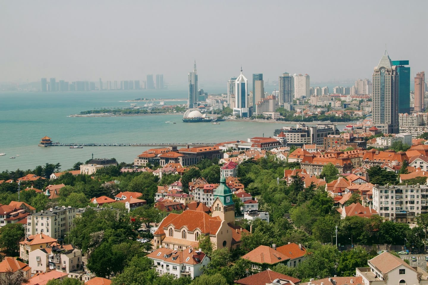 Coastal city with red roofs and modern skyscrapers near the sea.