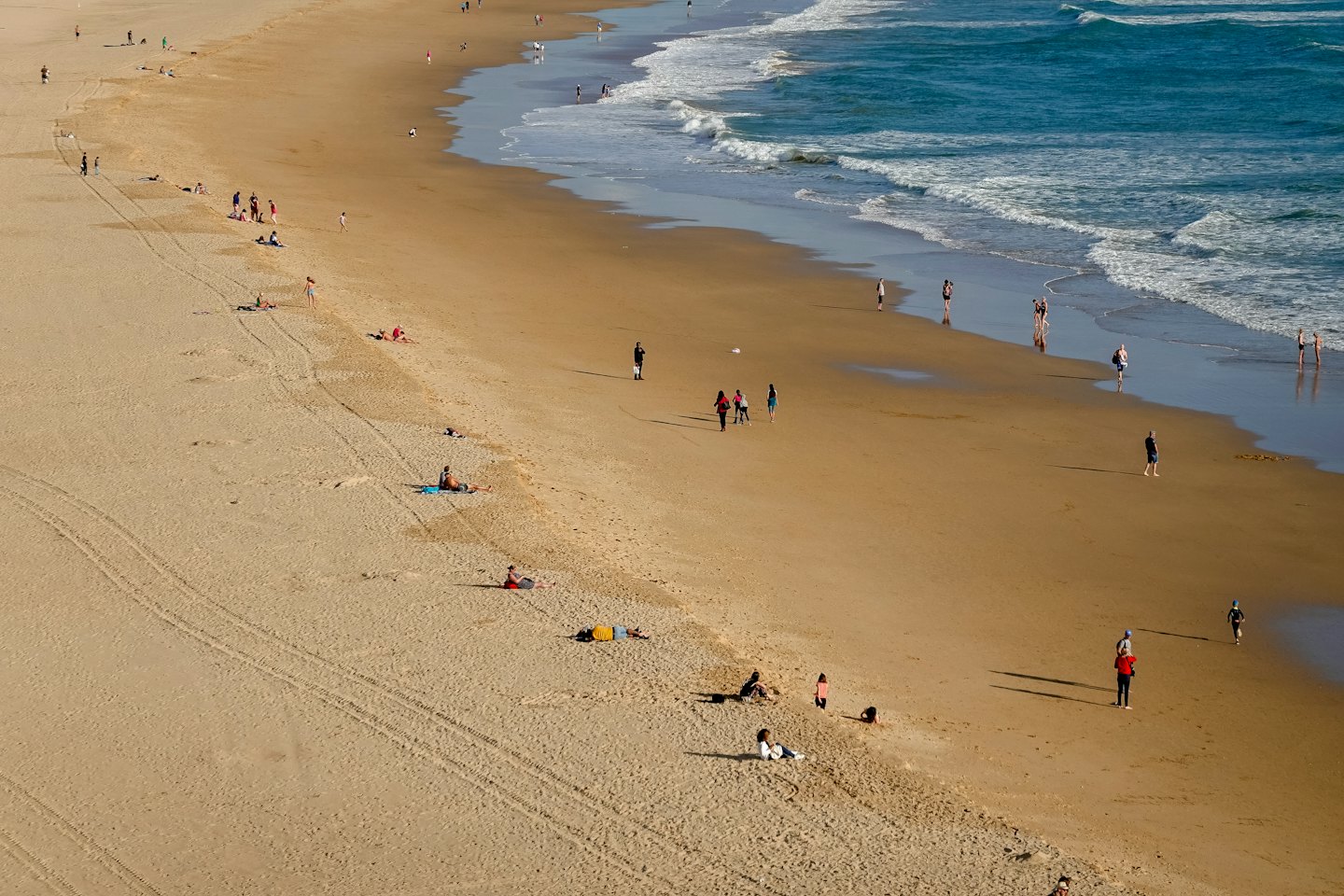 People enjoy a sunny day at a wide sandy beach.